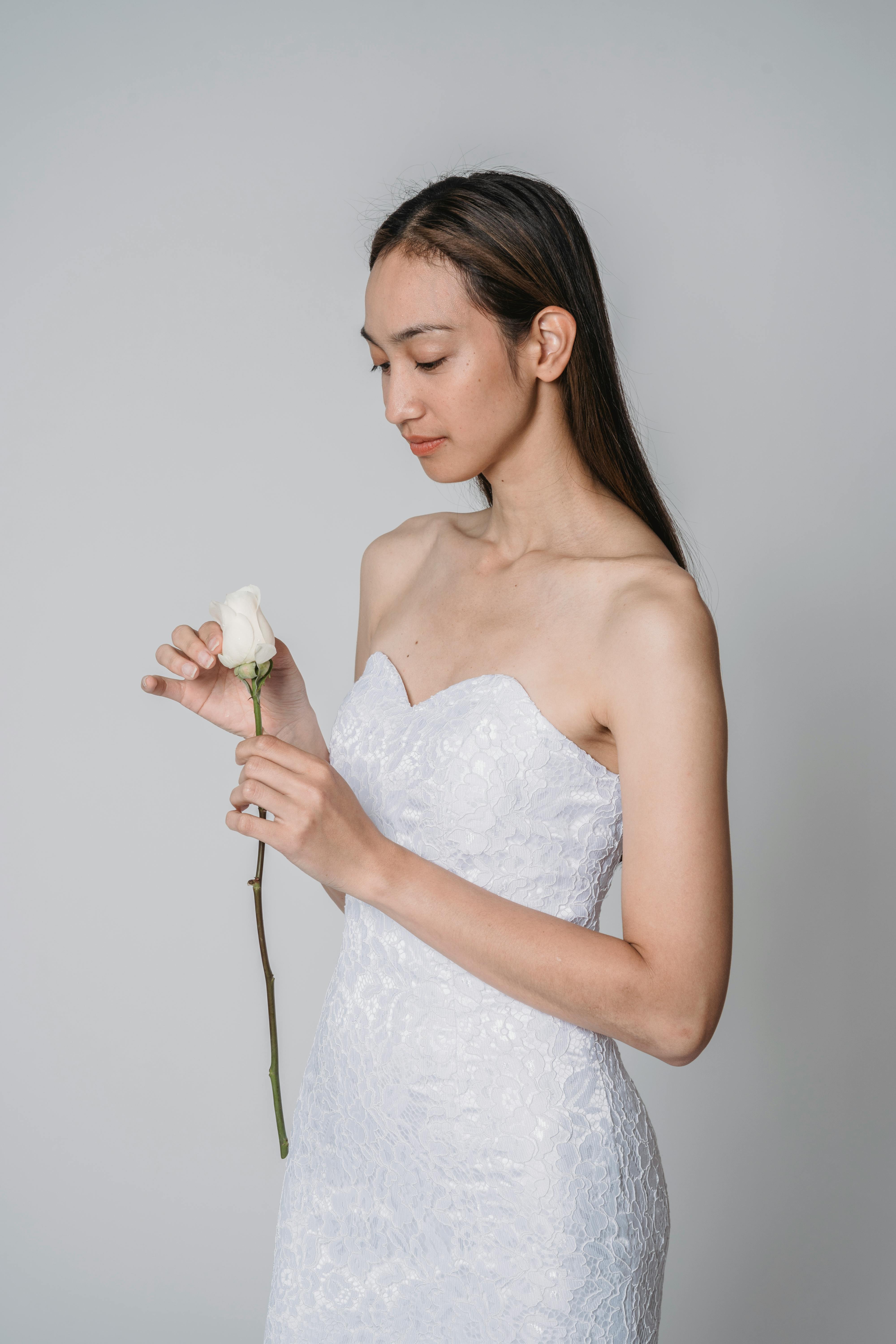 A serene bride in a white dress holding a single white rose against a subtle backdrop.