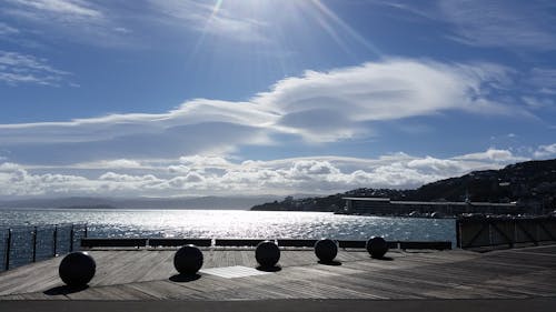 Five Balls Placed on Gray Wooden Platform Near Sea