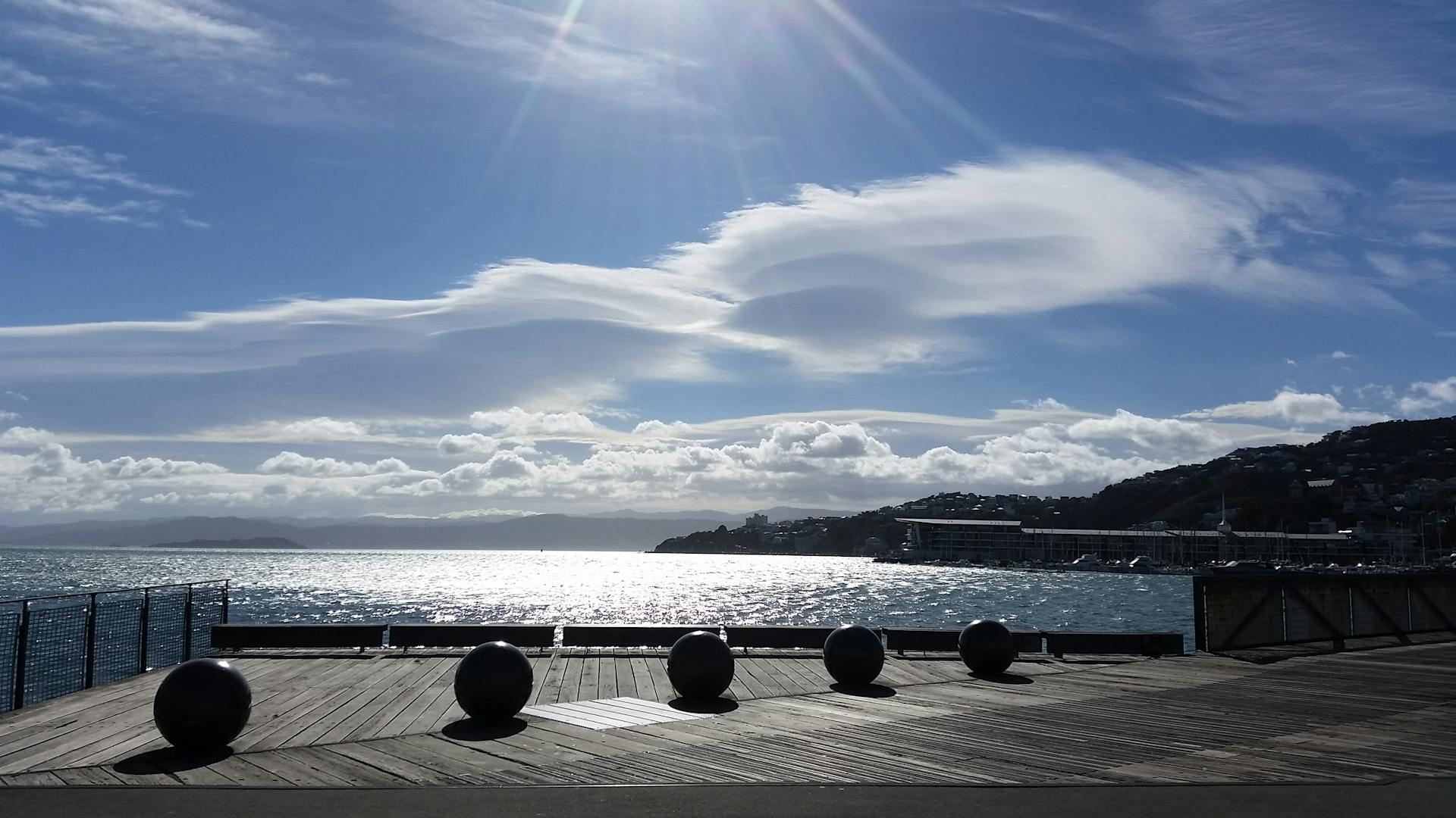 Scenic view of Wellington's waterfront with sunlit clouds and a clear blue sky.