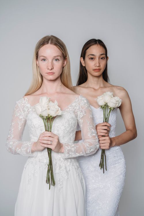 Free Two brides in stylish wedding dresses pose with bouquets in a studio setting. Stock Photo