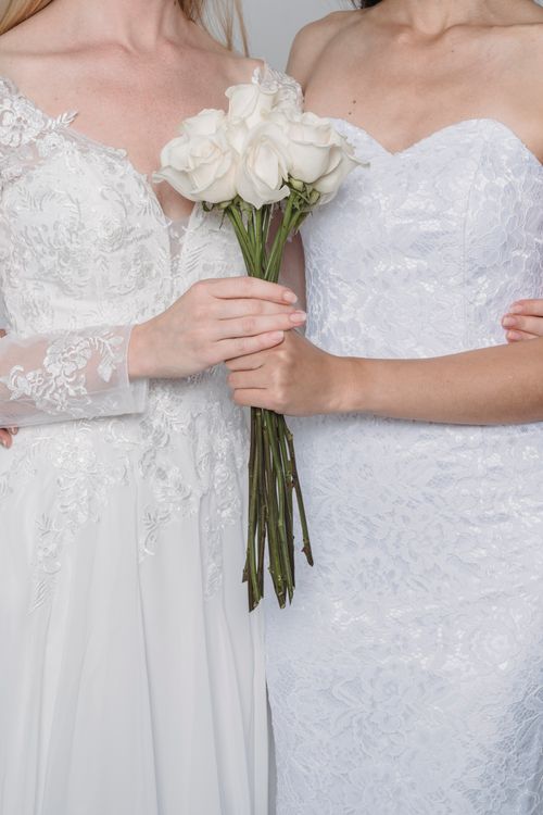 Free Two brides in lace gowns holding a bouquet of white roses, signifying love and commitment. Stock Photo