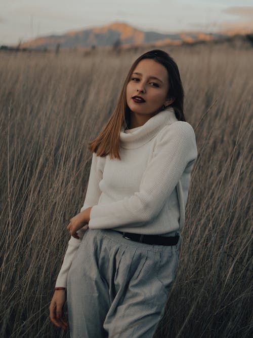Woman Wearing a White Sweater and Gray Pants Standing on a Grass Field