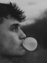 Grayscale Photo of Man Blowing a Bubble Gum