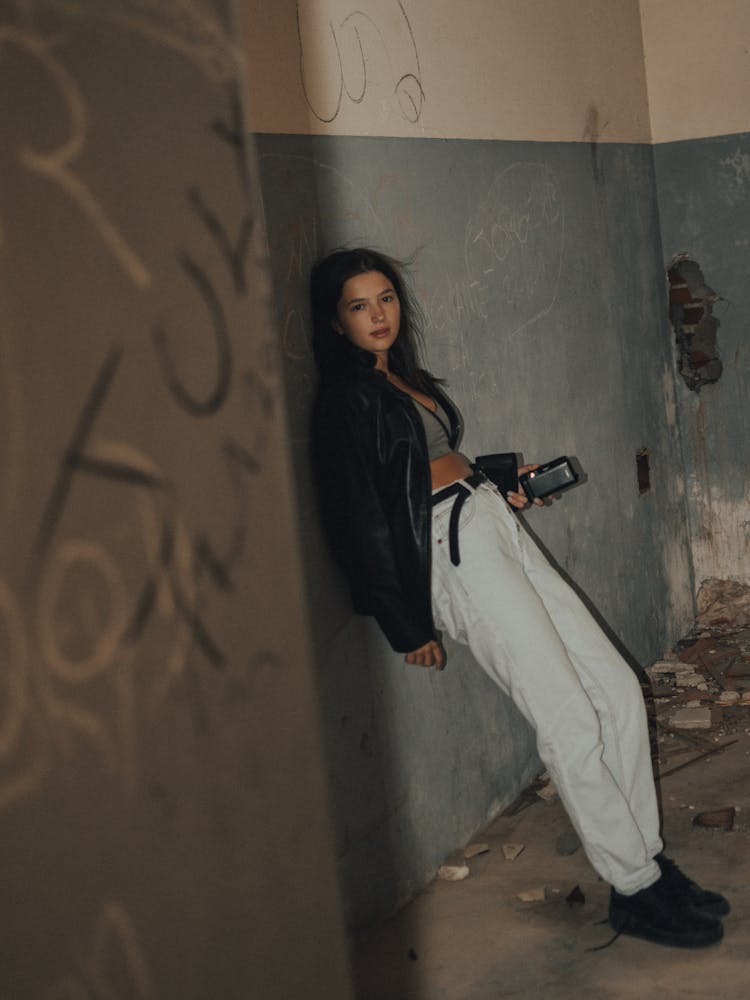 A Woman In Black Jacket And White Pants Leaning On The Wall