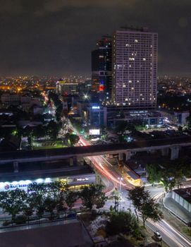 A dynamic aerial view of a brightly lit cityscape at night with light trails from traffic, showcasing urban life.