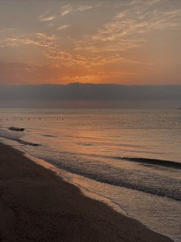 Serene dawn on a quiet beach with calm waves and a glowing sunrise.