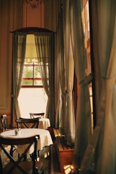 Classic restaurant interior featuring elegant curtains and wooden seating by large windows.