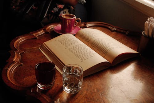 Free An Open Book Near the Drinking Glasses on a Wooden Table Stock Photo