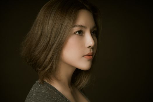 Side profile of an elegant woman posing with a dark background in a studio setting.