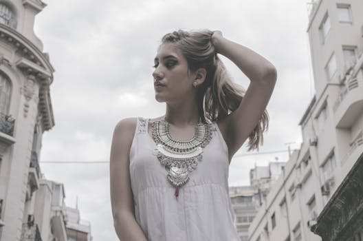 一位年轻女子身穿白色无袖连衣裙，戴着精致项链，在城市景观中自信地摆出姿势