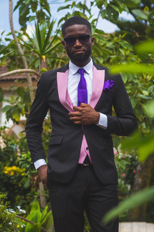 Free A confident man in a suit posing outdoors with greenery around him. Stock Photo