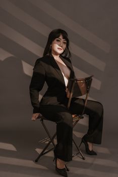 Stylish woman in black suit with hoop earrings poses elegantly in studio lighting.