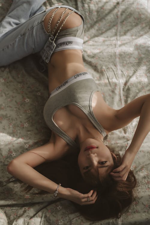 Free Woman in Gray Crop Top and Denim Jeans Lying on Bed Stock Photo