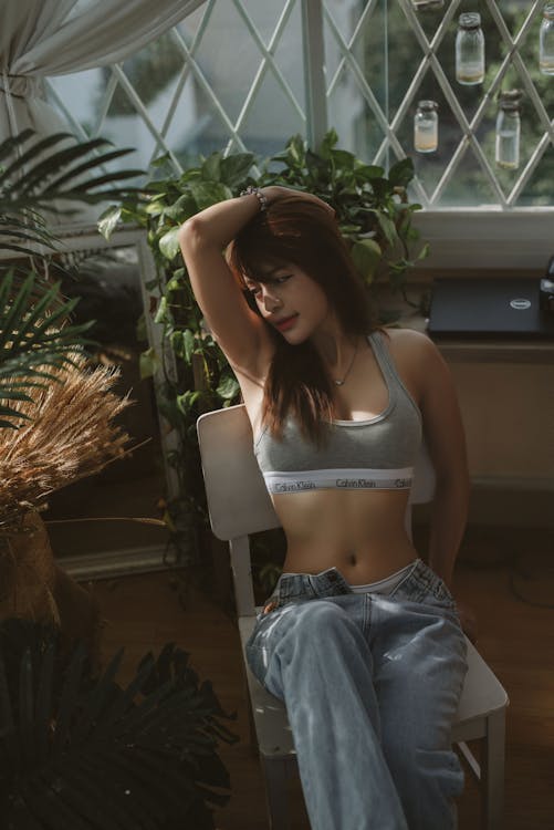 Woman in Gray Brassiere and Blue Denim Jeans Sitting on White Chair