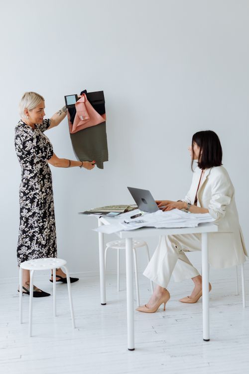 Free Two women discussing fabric samples in a modern, minimalistic workspace, highlighting creativity and collaboration. Stock Photo