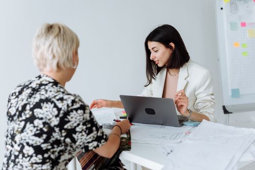 Free Two women collaborate in a modern office, using laptops and papers for planning. Stock Photo