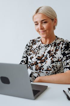 A woman smiling while working remotely on a laptop with a white background, embodying modern technology and remote work culture.