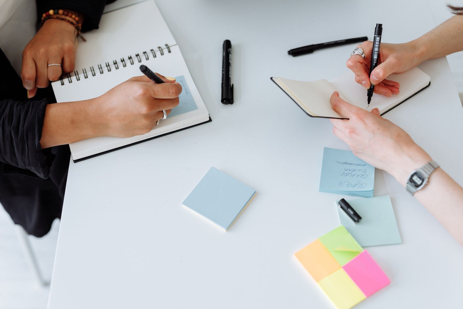 Two people writing notes in notebooks across a shared desk — photo by Thirdman on Pexels