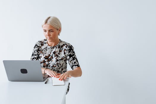 A focused woman works on her laptop in a bright, minimalist space, embodying remote work.