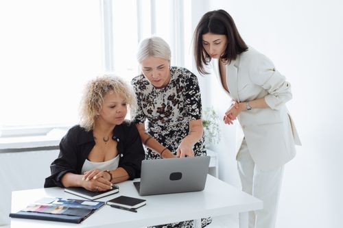 Free Three diverse women collaborating on a project with a laptop in a bright office. Stock Photo