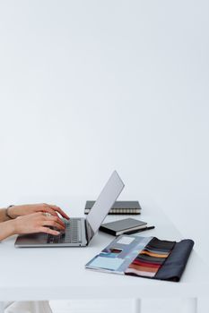 Minimalist workspace featuring fabric swatches, a laptop, and a person's hands typing, conveying business and creativity.