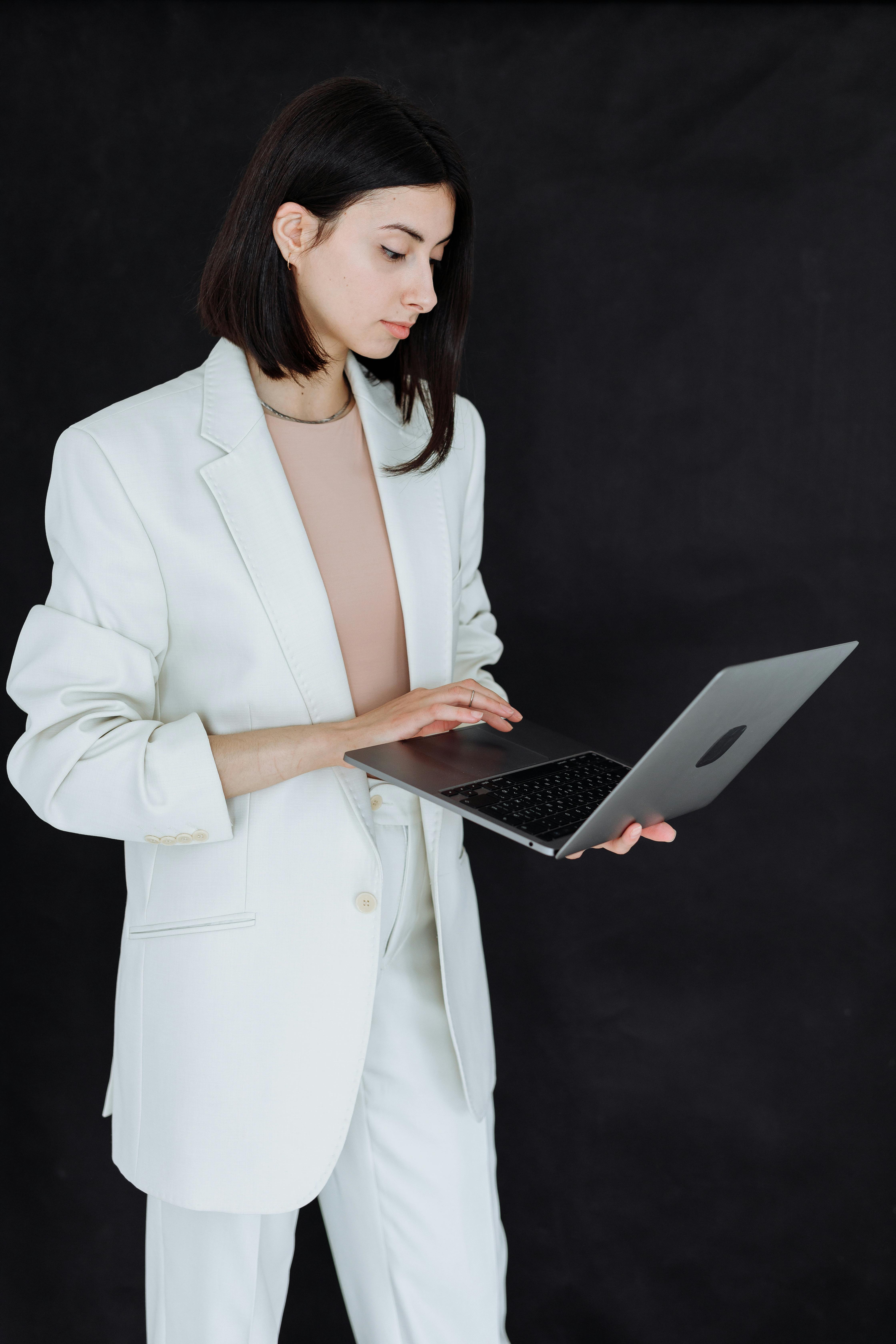 woman in white blazer holding a laptop