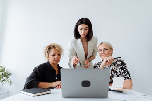 Free Three women collaborating on a project with a laptop in a bright office setting. Stock Photo
