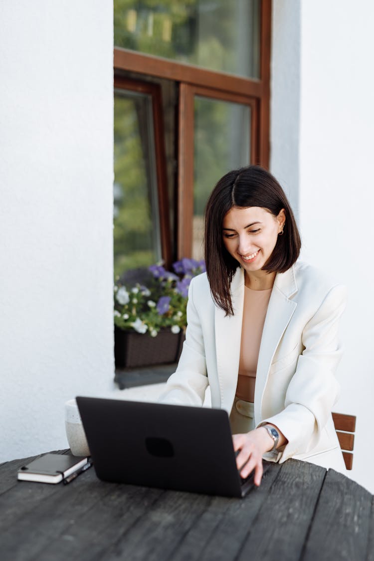 Woman In White Blazer Using Black Laptop On The Wooden Table