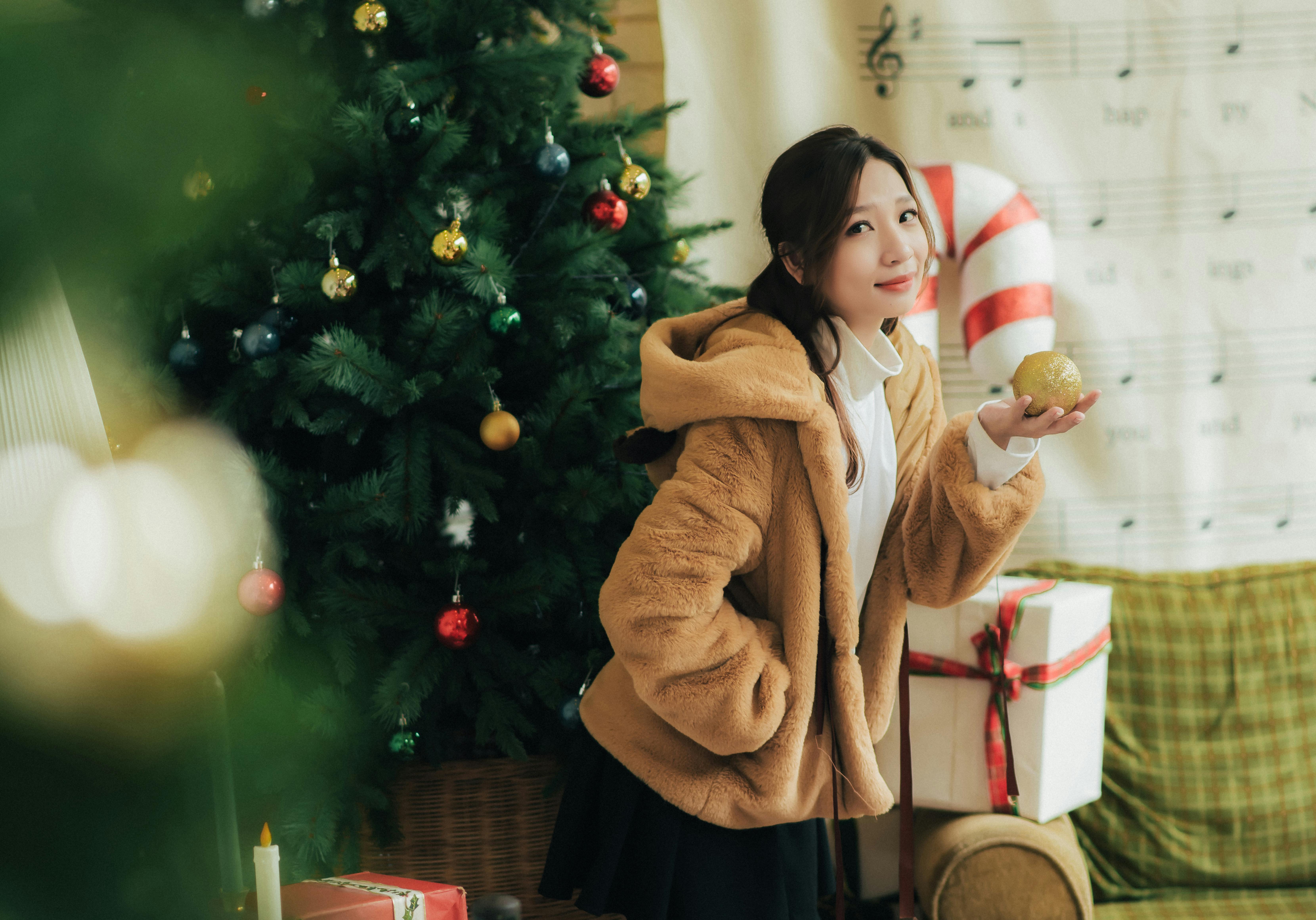 Woman in festive attire posing with a decorated Christmas tree and gifts, capturing holiday spirit.