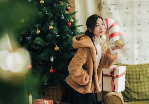 A Woman Standing Beside the Christmas Tree Holding an Ornament