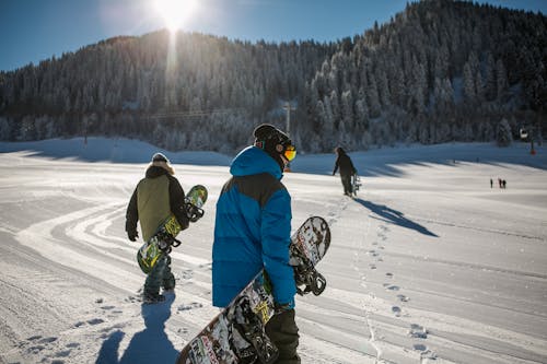 бесплатная Человек в синей зимней куртке с сноубордом под солнечным небом Стоковое фото