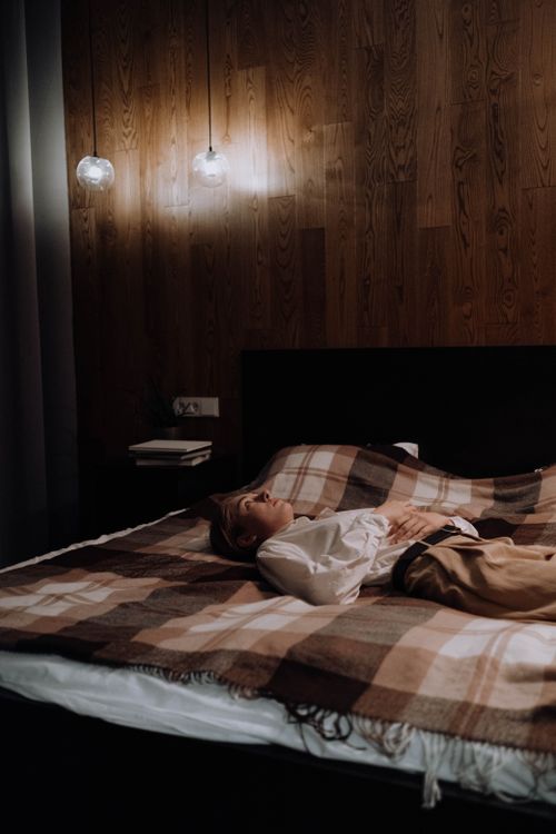 Free A woman lying on a bed in a cozy, stylish bedroom with wooden walls and ambient lighting. Stock Photo