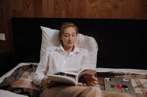 Free Woman Reading a Book While Lying on the Bed Stock Photo