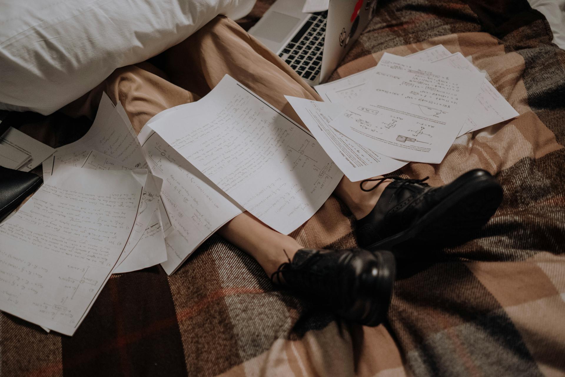 A cozy, messy workspace on a bed with papers and a laptop, depicting a freelancer's life.