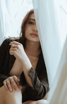 Intriguing portrait of a woman partially behind sheer curtains, emanating grace and mystery.