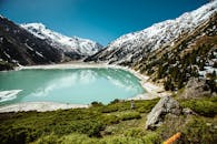 一名跑步者沿着宁静湖泊边的山间小道奔跑，湖面倒映着白雪皑皑的山峰