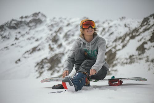 Person in Grey Hoodie Sitting on Snowboard