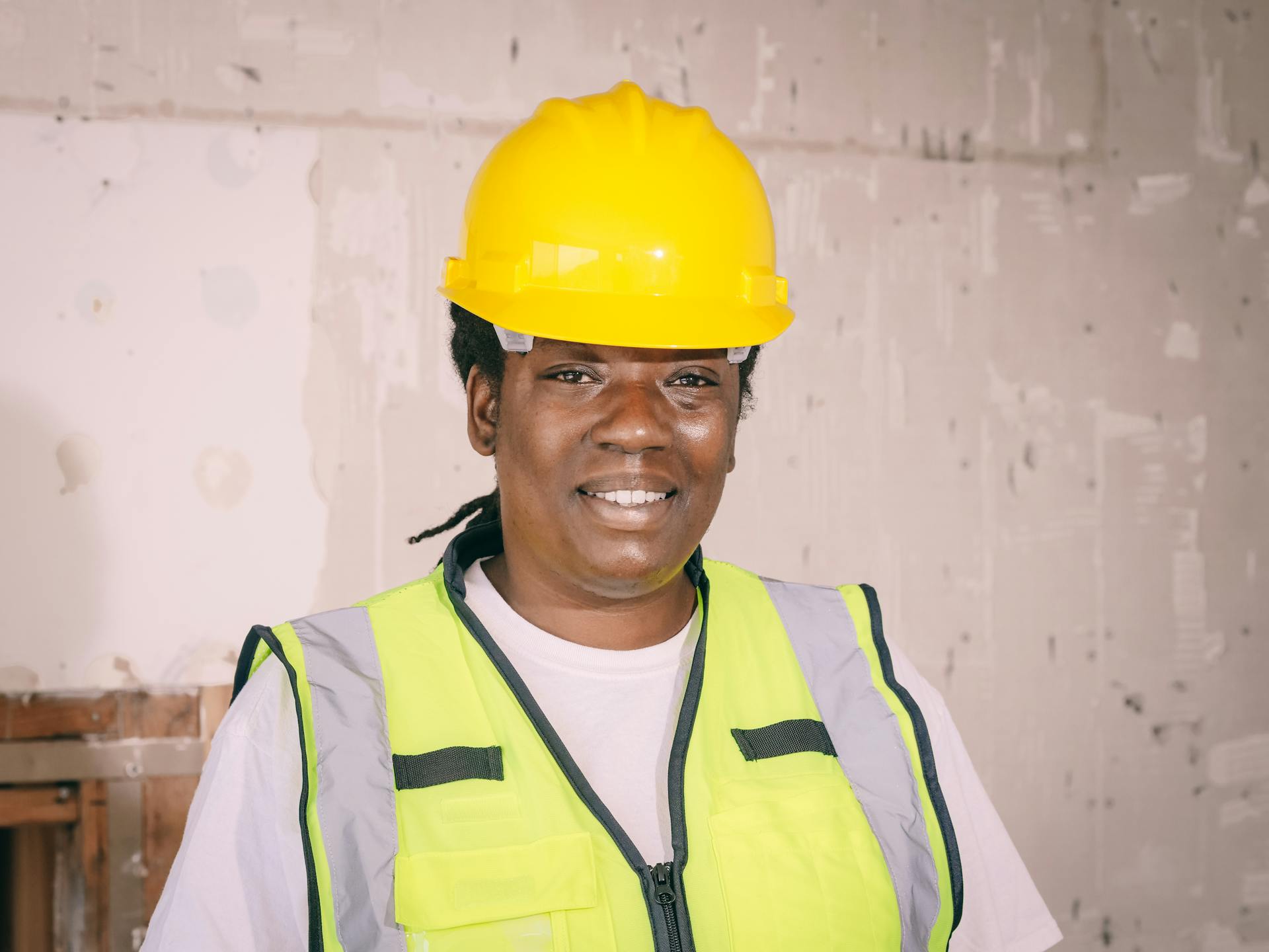 Smiling female engineer wearing safety gear and hardhat in an indoor construction setting.