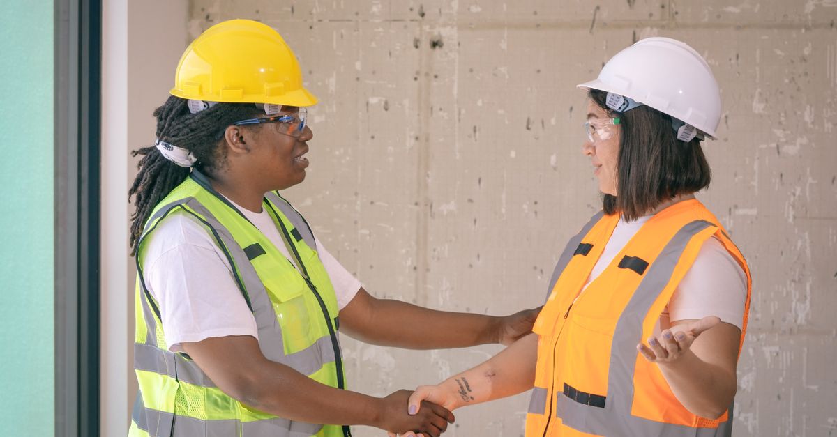 Two construction professionals in safety gear shaking hands on a job site