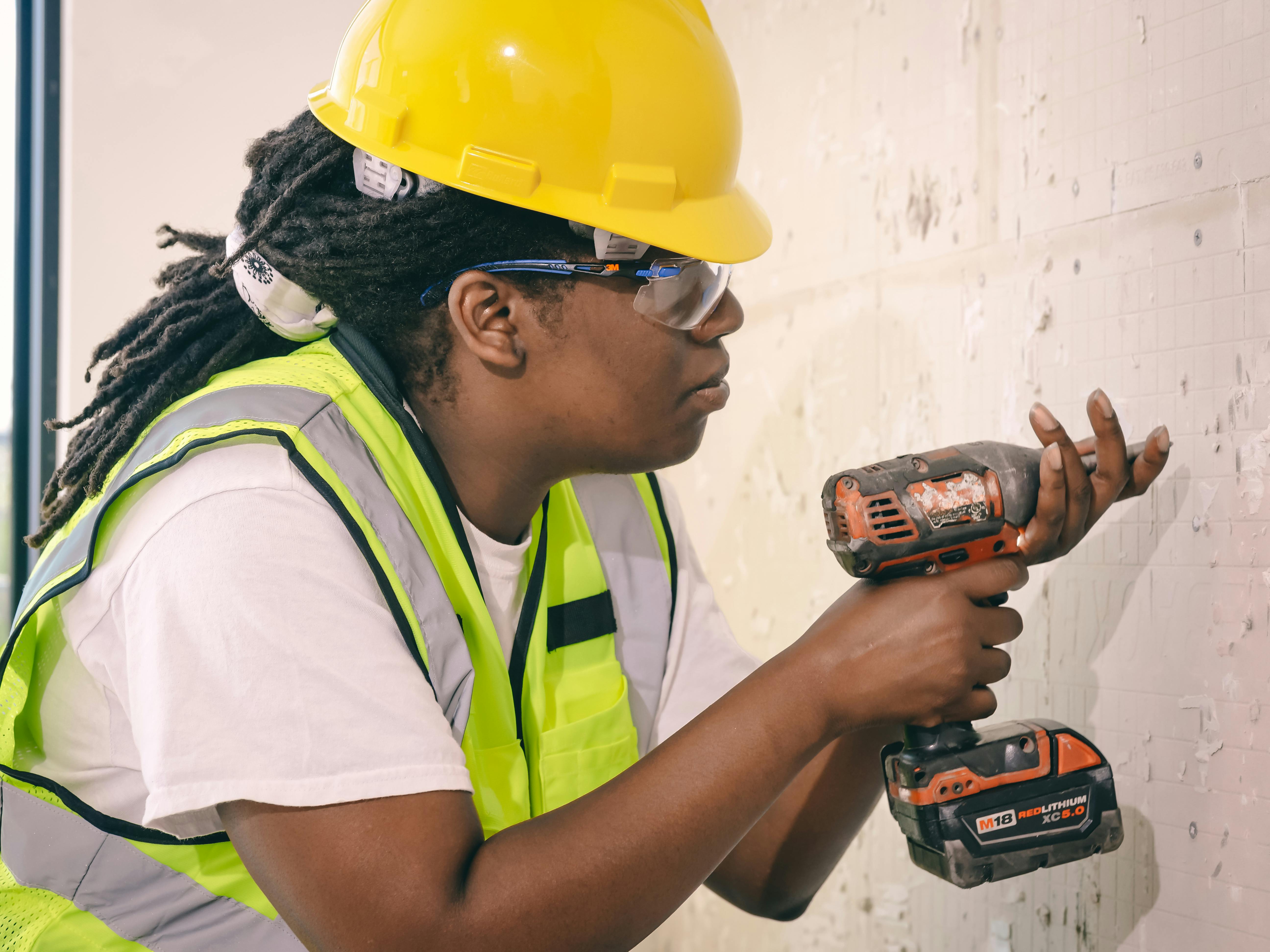 Free A female construction worker using a drill, wearing safety gear indoors. Stock Photo