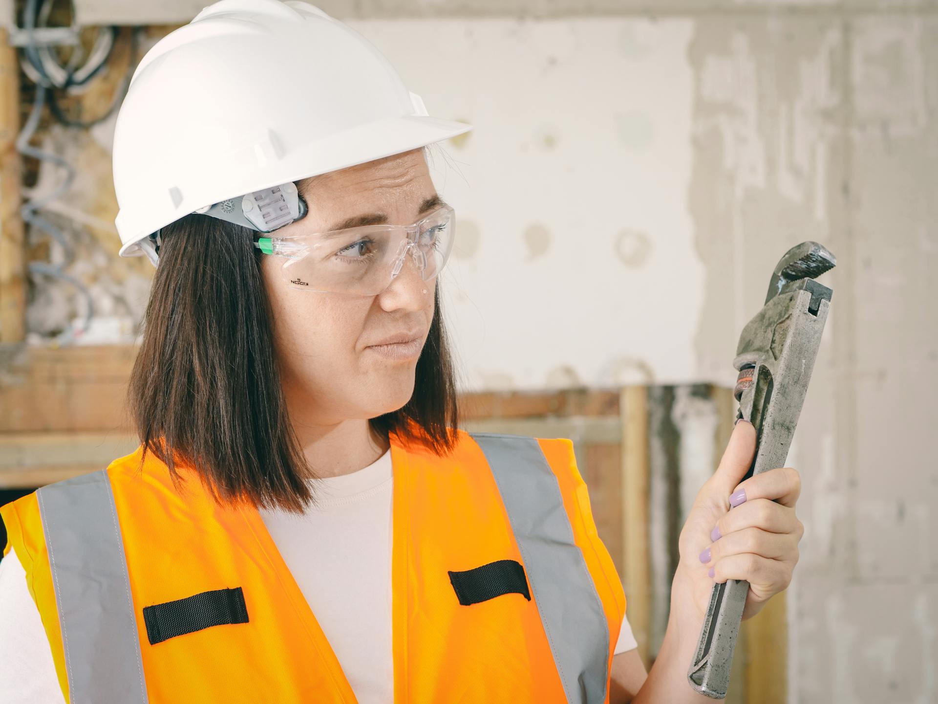 Caucasian woman in PPE holding a plumber's wrench indoors, focused on maintenance.