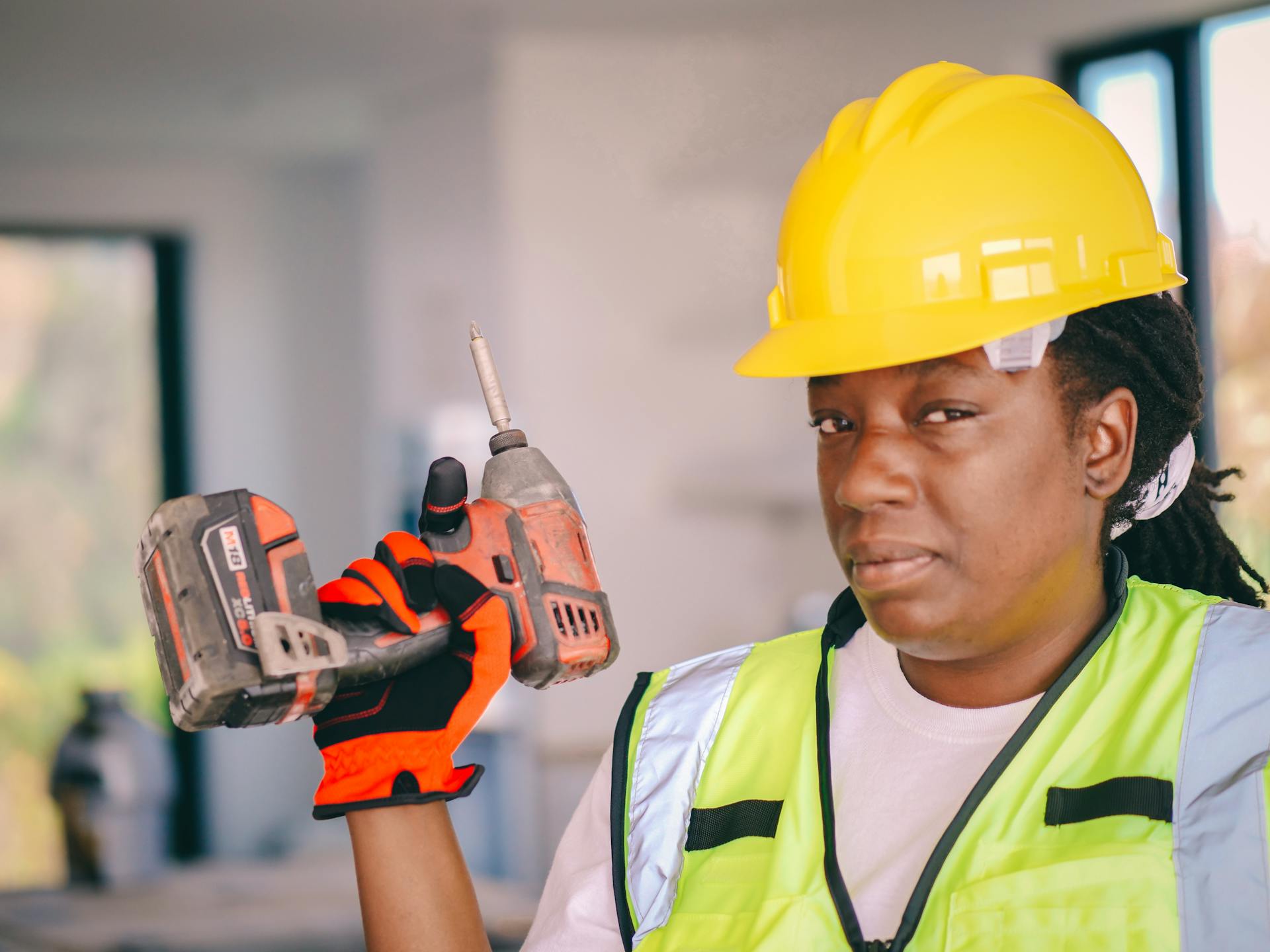 Black female construction worker with a drill, wearing safety equipment and hard hat.