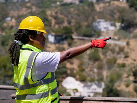 Black female safety inspector wearing PPE and hardhat pointing in outdoor setting.
