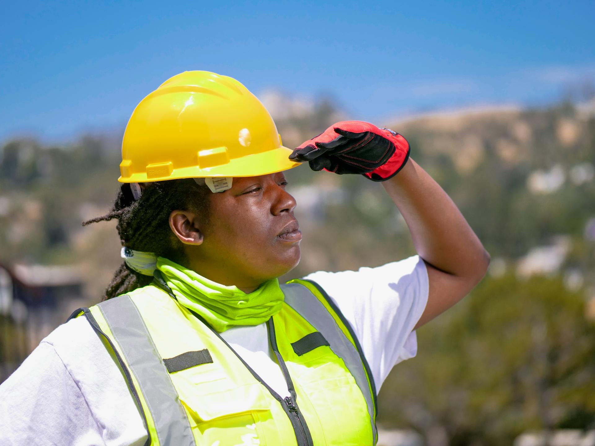 A professional woman wearing safety gear, hardhat, and reflective vest surveying outdoors.