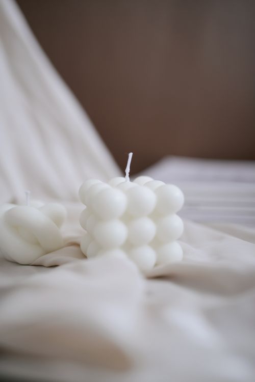 Free Minimalist white bubble candles placed on soft, neutral fabric, creating a serene atmosphere. Stock Photo