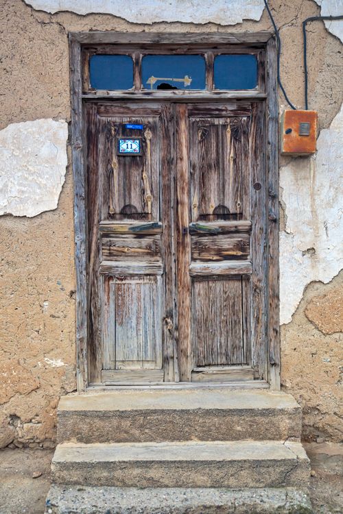 Free Close-up of an old, weathered wooden door on a rustic, peeling facade with concrete steps. Stock Photo