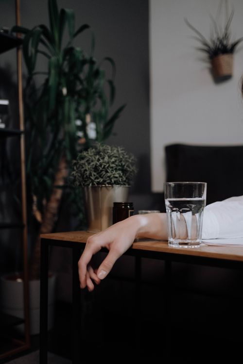 Free A serene indoor scene with a person's hand resting on a table with a glass of water. Stock Photo