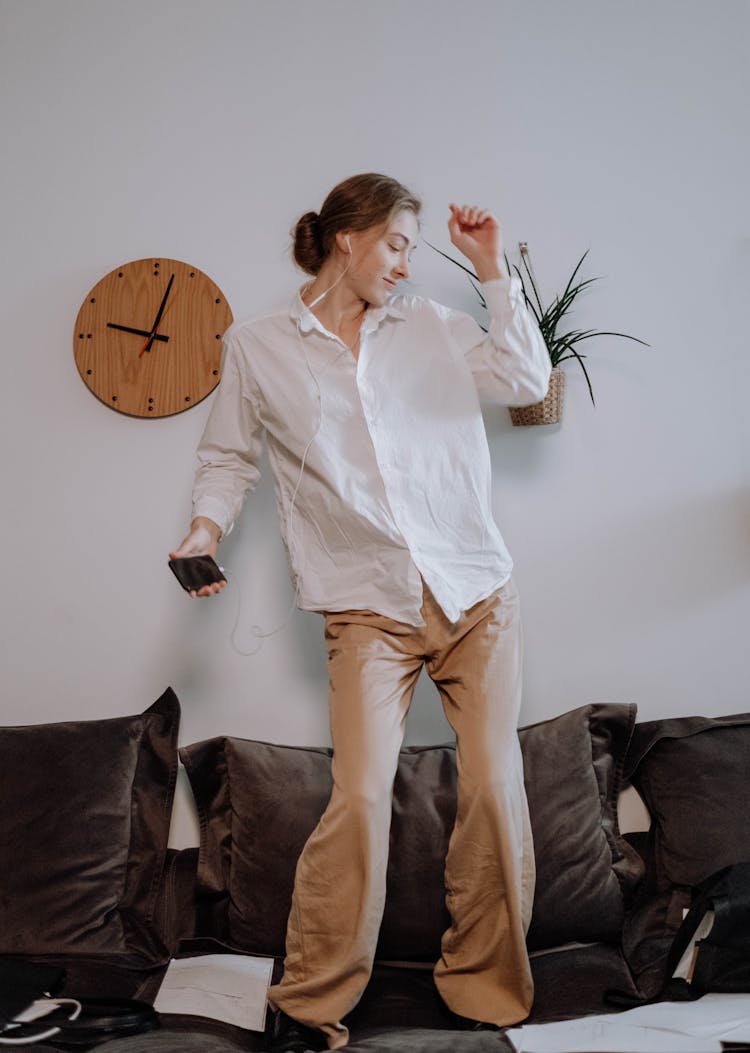 Woman Standing On A Couch Listening To Music And Dancing