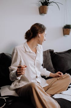 Young woman working on a couch in casual attire while listening to music.