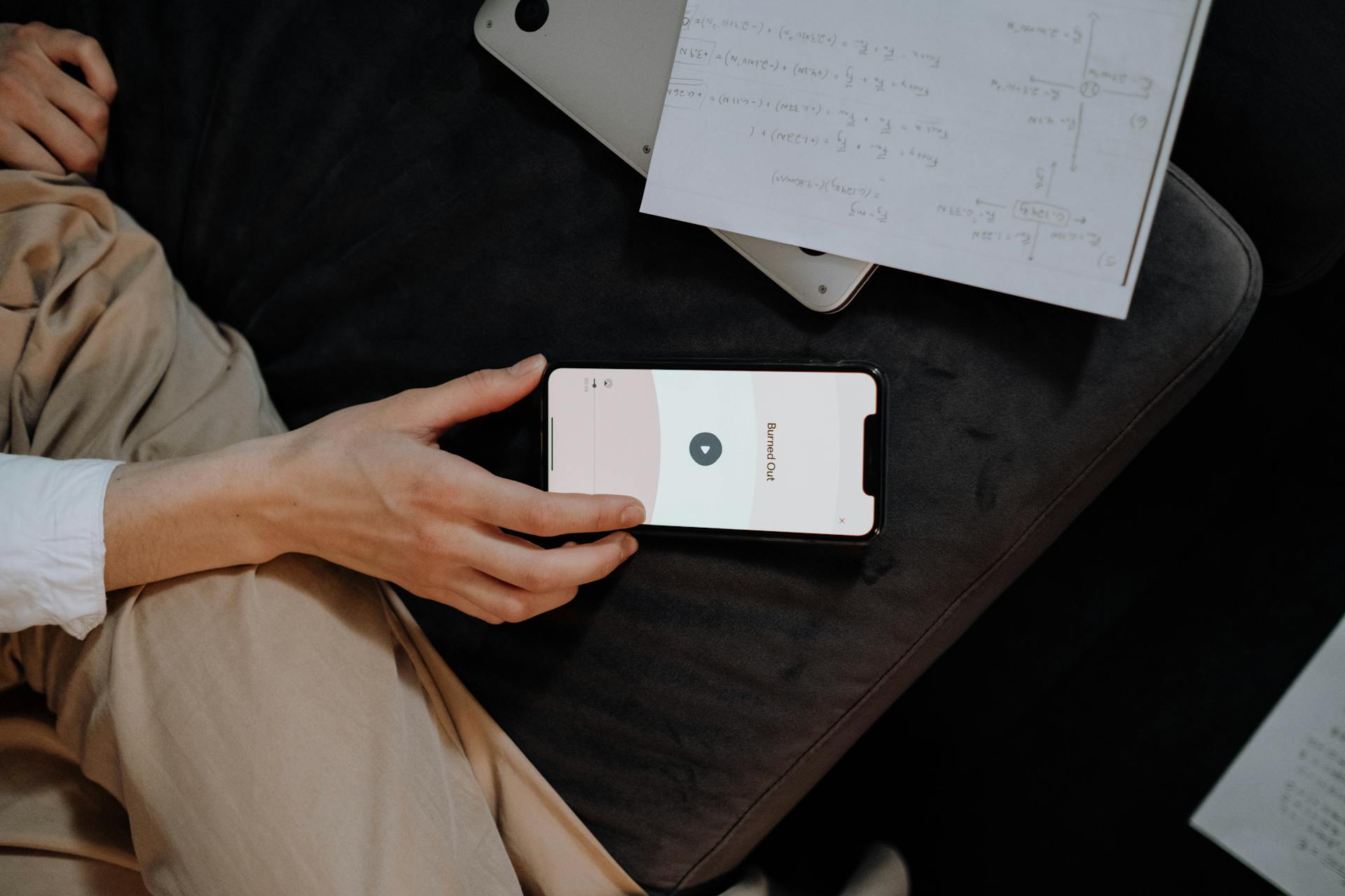 A hand holding a smartphone displaying an app, surrounded by notes and a laptop.